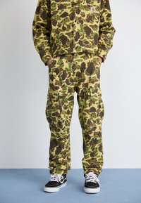 Camouflage-patterned outfit in shades of green and brown, made from durable fabric. Features a button-up jacket and cargo pants with pockets.