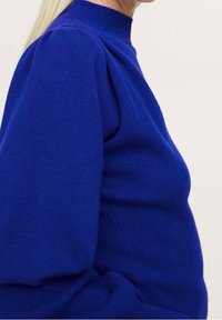 Pull col montant bleu roi avec texture côtelée et manches bouffantes, silhouette ajustée, tissu doux et lignes épurées.