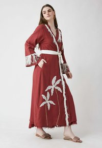 Kimono long bordeaux avec des manches à franges blanches et une ceinture. Présente des motifs en dentelle blanche en forme de feuilles et des poches. Tissu doux et fluide.
