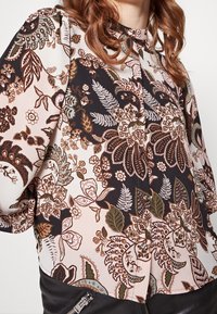 Blusa floreale con collo alto e bottoni, caratterizzata da una combinazione di colori scuri e pastello, motivi intricati e materiale morbido.