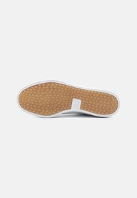 White sneaker sole with a textured light brown rubber surface, featuring a wavy pattern and a small logo near the heel.