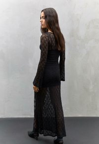 Schwarzes Spitzenkleid mit langen, ausgestellten Ärmeln und einem taillierten Oberteil sowie einem durchsichtigen, fließenden Rock. Die Textur ist kompliziert und zart.