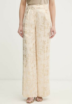 Beige hoch taillierte, weit geschnittene Hose mit einem dezenten abstrakten Strukturmuster, getragen zu offenen goldfarbenen Sandalen mit Riemchen.