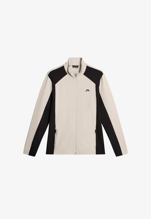 Light beige zip-up jacket with black side panels, high collar, long sleeves, and logo on the chest. Smooth, lightweight fabric.