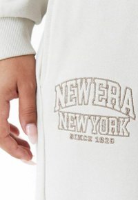 Cremefarbener Sweatshirt mit gerippten Bündchen, versehen mit braunem Stickdesign "NEW ERA NEW YORK" und "SINCE 1920" darunter. Weicher Stoff, lässiges Design.