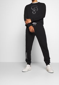 Czarny komplet z bluzą i spodniami dresowymi z grafiką postaci w okularach przeciwsłonecznych. Bia�łe sznurki oraz napisy po bokach. Casualowy design.