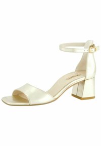 Sanda s otevřenou špičkou a blokovým podpatkem v lesklém slonovinovém materiálu, s bezpečným zapínáním kolem kotníku a minimalistickým designem. Hladká textura s jemným prošitím.