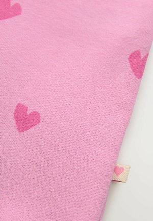 Tissu rose avec une texture douce et des motifs de cœurs dispersés. Une petite étiquette avec un accent en forme de cœur est visible sur le bord.