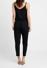Mono negro con espalda descubierta y tirantes finos. Presenta una cintura elástica y perneras estrechas. Se lleva con sandalias de tacón cuadrado.