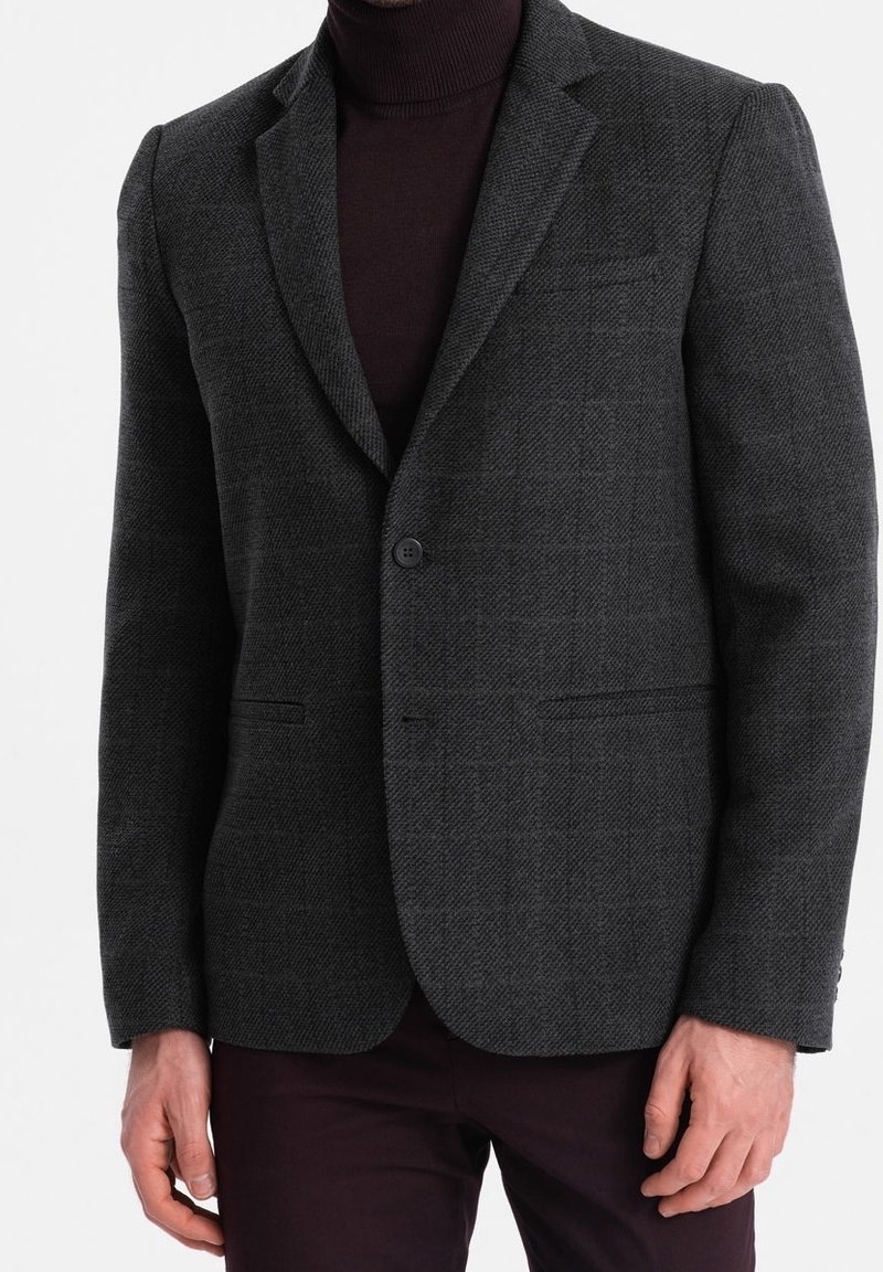 Ciemnoszara marynarka o fakturowanej tkaninie, dopasowany krój, dwie przednie kieszenie oraz pojedyncze zapięcie na guzik. Noszona na ciemnym golfie.