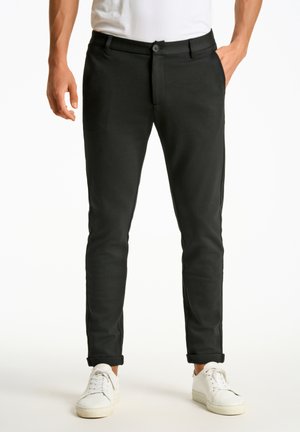 Svarta slim-fit byxor med slät front och knäppning, med sidofickor och uppvikta muddar, kombinerat med vita sneakers.