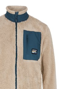 Giacca in fleece beige con una tasca sul petto in teal con zip e un'etichetta del logo. Presenta un colletto alto e un tessuto testurizzato per il calore.