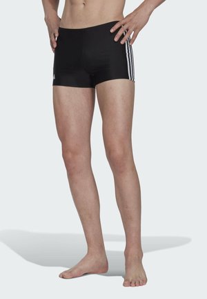 Pantaloni da bagno neri realizzati in tessuto liscio, con tre strisce bianche su ciascun lato, dal design aderente e di lunghezza media fino alla coscia.