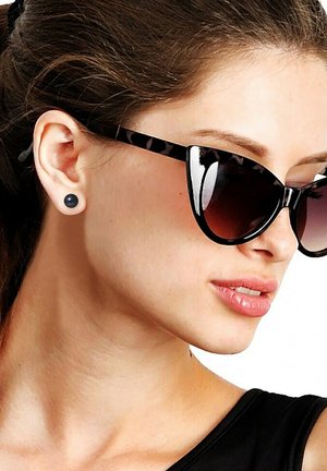Des lunettes de soleil noires en forme d'œil de chat avec des accents léopard, des verres foncés et des boucles d'oreilles rondes noires en clou. Une peau lisse avec une légère brillance.