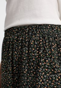 Schwarte Blumenkleid aus leichtem Stoff, mit einem gerafften Taillenbund und cremefarbenen, orangen und grünen Blumenmustern.