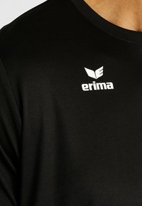 T-shirt de sport noir avec un col rond, fabriqué en tissu texturé. Présente un logo "erima" blanc et des détails d'accent.