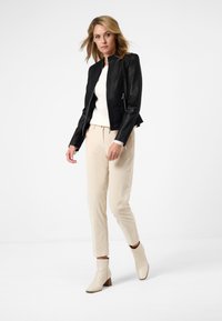 Svart skinnbombarjacka med en figursydd design, kombinerad med krämfärgade byxor och beige klackboots som når ankeln, vilket ger en elegant silhuett.