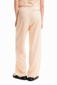 Pantalons larges de couleur pêche clair avec un motif floral subtil, dotés d'une taille élastique et de poches latérales, associés à des chaussures à plateforme noires.