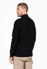 Maglione nero a maglia con colletto alto, texture a coste e maniche lunghe. La vista posteriore mostra un design aderente con taglio dritto all'orlo.