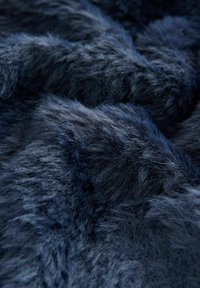 Tessuto in pelliccia sintetica blu navy con una superficie morbida e testurizzata. Le fibre sono spesse e densamente unite, creando un aspetto ricco e lussuoso.