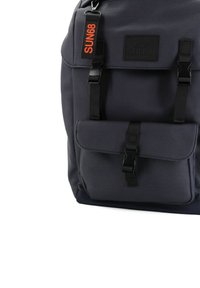 Zaino grigio realizzato in tessuto testurizzato con spalline regolabili, una tasca frontale e un'etichetta con la scritta "SUN68" in arancione, dotato di accessori neri.