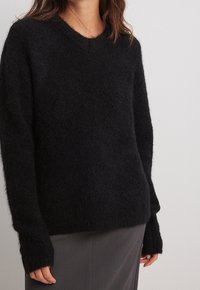 Pull noir à col en V surdimensionné en matière douce et duveteuse avec manches longues. Il présente une coupe décontractée et un design minimaliste.