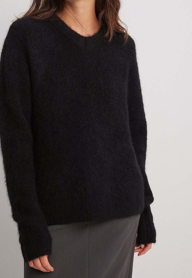 Pull noir à col en V surdimensionné en matière douce et duveteuse avec manches longues. Il présente une coupe décontractée et un design minimaliste.