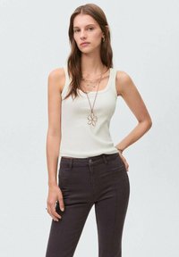 Top de tirantes blanco acanalado con tirantes anchos, combinado con jeans ajustados de color gris oscuro. Los accesorios incluyen collares en capas y pendientes de aro.