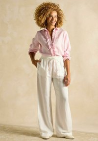 Hele roosa linane särk, millel on volangidega detailid ja nööbid, kombineeritud valgete laiade pükstega, millel on elastne vöökoht ja nöör.