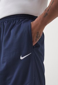 Tumesinine lühikesed püksid, millel on võrgust tekstuur, elastne vöökoht ja väike valge Nike logo. Omab küljetaskuid säilitamiseks.