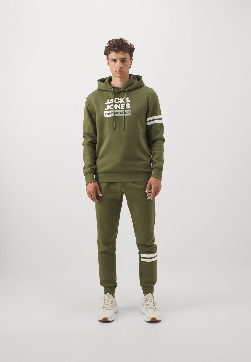 Grüne Kapuzenjacke und passende Jogginghosen aus weichem Stoff. Mit weißem Text und Streifen. Rundhalsausschnitt, verstellbare Kapuze und anliegende Bündchen.