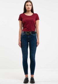 Camiseta burdeos con cuello redondo, combinada con jeans ajustados de color azul oscuro. El conjunto se complementa con un cinturón negro y zapatos negros gruesos.
