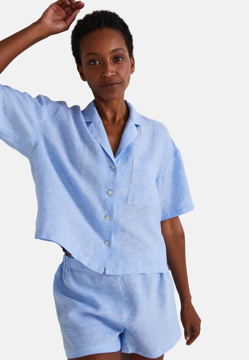 Chemise en lin bleu clair à manches courtes avec des boutons et une poche, assortie à un short. Texture douce, coupe décontractée, design casual.