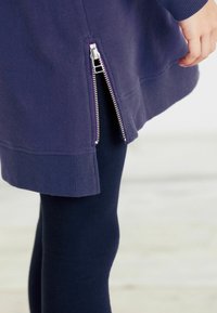 Námořnická mikina se žebrovanými manžetami a spodním lemem, s postranním stříbrným zipem. V kombinaci s námořnickými legínami, což vytváří sladěný vzhled.