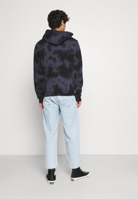 Felpa tie-dye nera e blu marina con un ampio cappuccio, polsini e orlo a costine, abbinata a jeans azzurri chiari e sneakers alte nere.