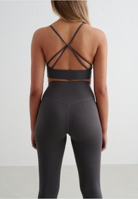 Gray athleisure set featuring a tank top with crisscross straps and high-waisted leggings. Smooth fabric with a matte finish and no visible logos.