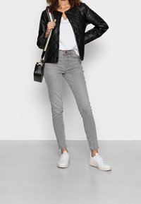 Giacca di pelle trapuntata nera, t-shirt bianca, jeans grigi slim-fit e sneakers bianche. Porta una borsa a tracolla nera con hardware dorato.