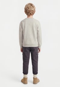 Enfant aux cheveux blonds bouclés, vu de dos, portant un sweat-shirt gris clair, un pantalon cargo foncé, des chaussettes beiges et des bottes en daim marron clair.