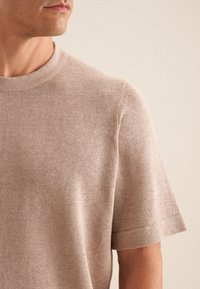 T-shirt a maniche corte color marrone chiaro in maglia, con collo a giro e polsini a costine, tessuto leggermente texturizzato, design aderente e finitura pulita.