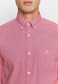 Rood-wit geruit overhemd met een button-down kraag, korte mouwen en witte knopen; heeft een zak met een logodetail.