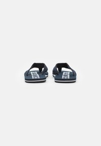 Marine flip-flops med teksturerede stofremme, flade såler og hvid branding på fodsålen. Minimalistisk design og afrundet form.
