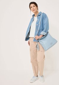 Világoskék velúr táska bojtokkal, amelyet farmerdzsekivel, fehér csíkozott toppal és bézs cargo nadrággal viselnek. A szettet laza sportcipők egészítik ki.