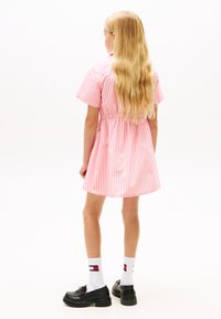 Ροζ και λευκό φόρεμα με ρίγες, κοντά μανίκια και ελαστική μέση. Μαύρα παπούτσια και λευκές κάλτσες με λογότυπο. Μακριά μαλλιά που ρέουν στην πλάτη.