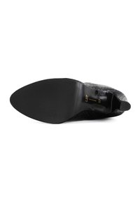 Sola di scarpa nera con tacco, caratterizzata da un motivo testurizzato e intrecciato. Presenta una punta affilata e una finitura liscia e lucida nell'area del tacco.