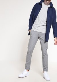 Námořnicky modrý voděodolný kabát přes světle šedý svetr; světle šedé elegantně střižené kalhoty; bílé tenisky; hladká textura; střední střih; neformální design.