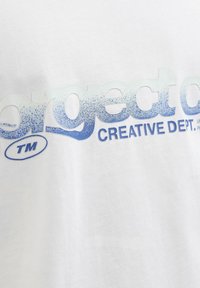 Λευκό ύφασμα με μπλε κειμενικό βαθμιαίο χρώμα που γράφει «biggest CREATIVE DEPT.» και μικρό σύμβολο «TM» σε οβάλ σχήμα.