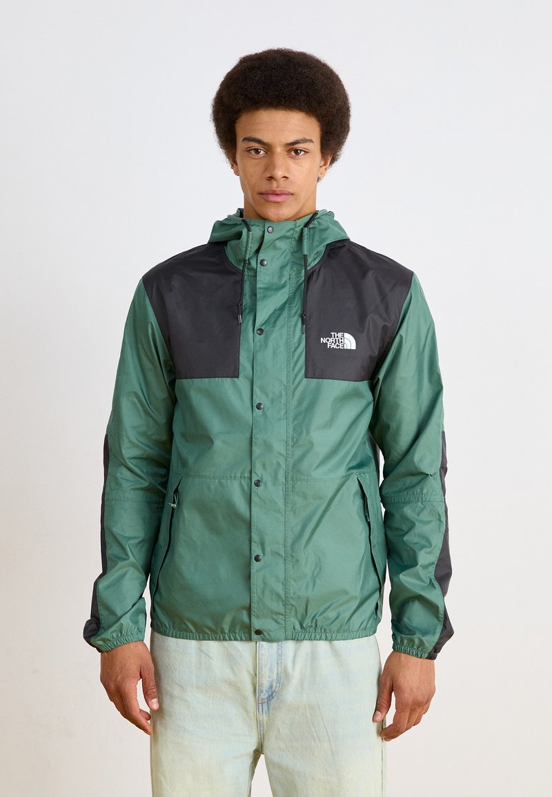Grüne und schwarze Windjacke mit Kapuze, Druckknöpfen und elastischen Bündchen. Mit Logo auf der Brust und seitlichen Taschen.
