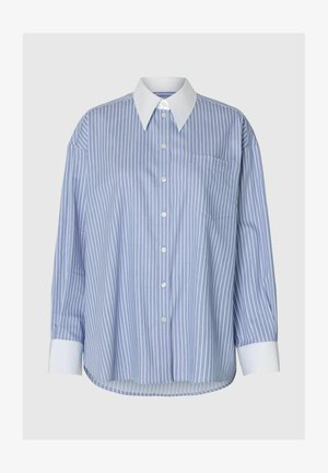 Sinivalkoraidallinen nappipaita, jossa on klassinen kaulus ja pitkät hihat. Siinä on yksi rintatasku ja kaareva helma.