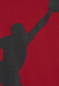 Tela roja con una textura suave que presenta la silueta grande y negra de una persona saltando, enfatizando la acción de alcanzar hacia arriba.