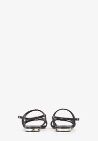 Sandali in pelle nera con cinturini eleganti, punta arrotondata e dettagli metallici su una suola piatta. Il design presenta dettagli minimalisti.